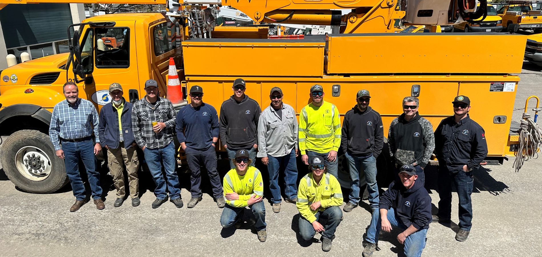 Group picture of TDPUD linemen and electric team, standing in front of a yellow bucket truck