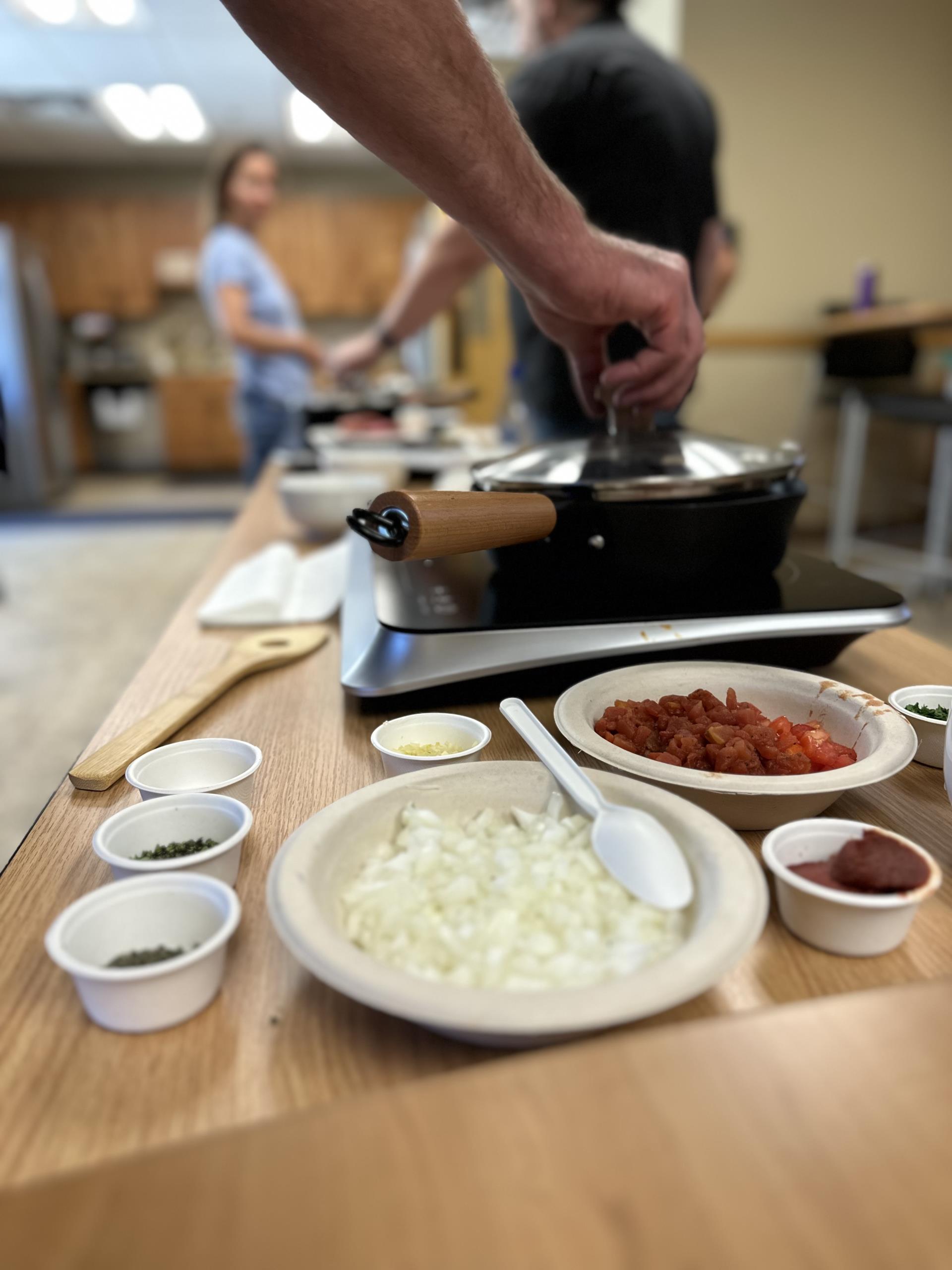 A person holding the top of the lid of a pan on an induction cooktop in TDPUD's induction cooking class