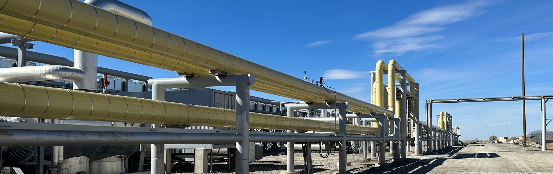 Photo of a geothermal plant, yellow pipes running horizontally across the picture