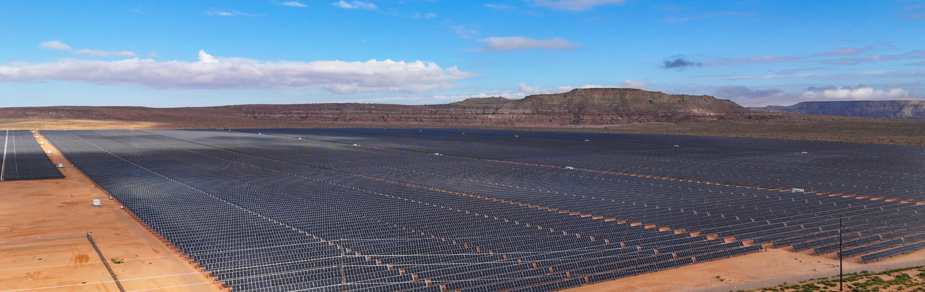 Aerial photo of Red Mesa Tapaha Solar Farm. Picture shows hundreds of rows of solar panel, with a butte in the distance, and a clear blue sky above